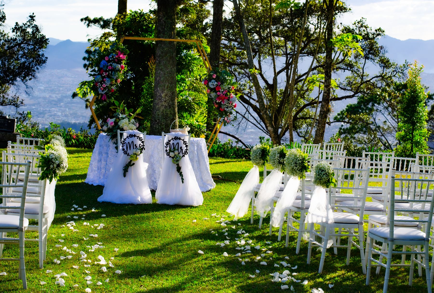 White chairs and a flower arch arranged for an outdoor ceremony